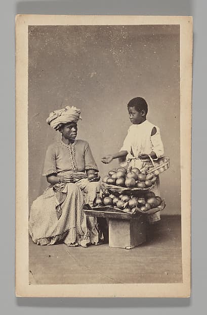 [Studio Portrait: Seated Woman and Standing Boy Street Vendors with Vegetable Baskets, Brazil], by Christiano Junior