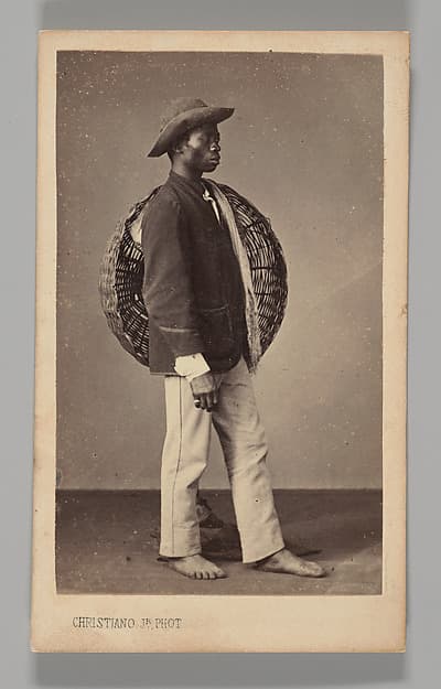 [Studio Portrait: Male Street Vendor Standing in Profile Holding Basket, Brazil], by Christiano Junior