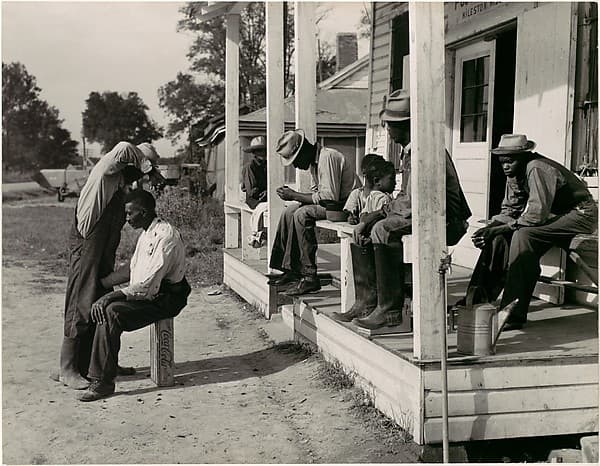 [Haircutting in Front of General Store and Post Office on Marcella Plantation, Mileston, Mississippi], by Marion Post Wolcott