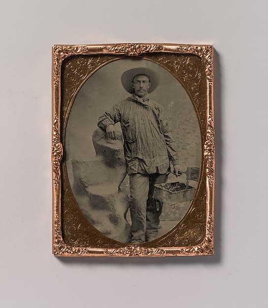 [Workman Holding Brush and Rectangular Tray, Arm Resting on Fake Rock], by Unknown