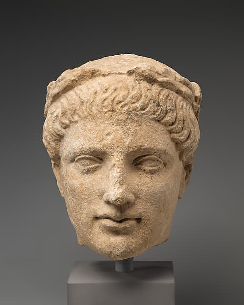 Limestone head of beardless male votary with wreath of leaves