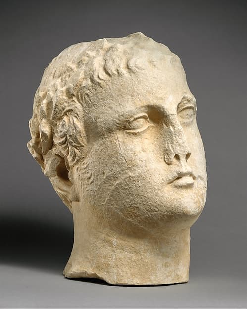 Limestone head of beardless male votary with wreath of leaves